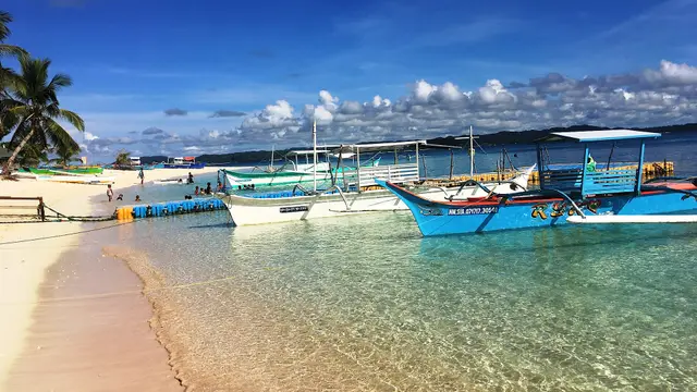 Blue outrigger bangka boats moored in clear shallow water along the white-sand beach of Daku Island, Siargao.