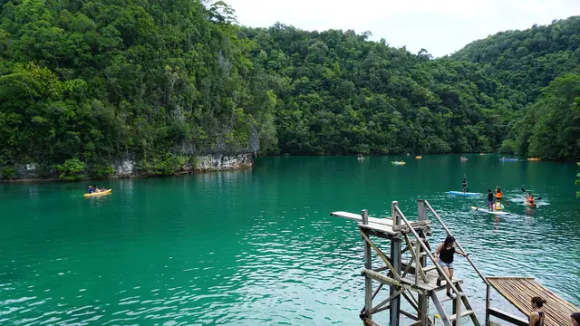 Emerald-green water of Sugba Lagoon in Del Carmen with a wooden diving platform, kayakers and forested limestone hills.